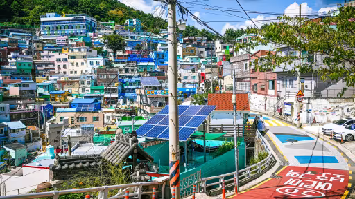 Arrays of solar panels are visible atop buildings in a colorful city on a hill.